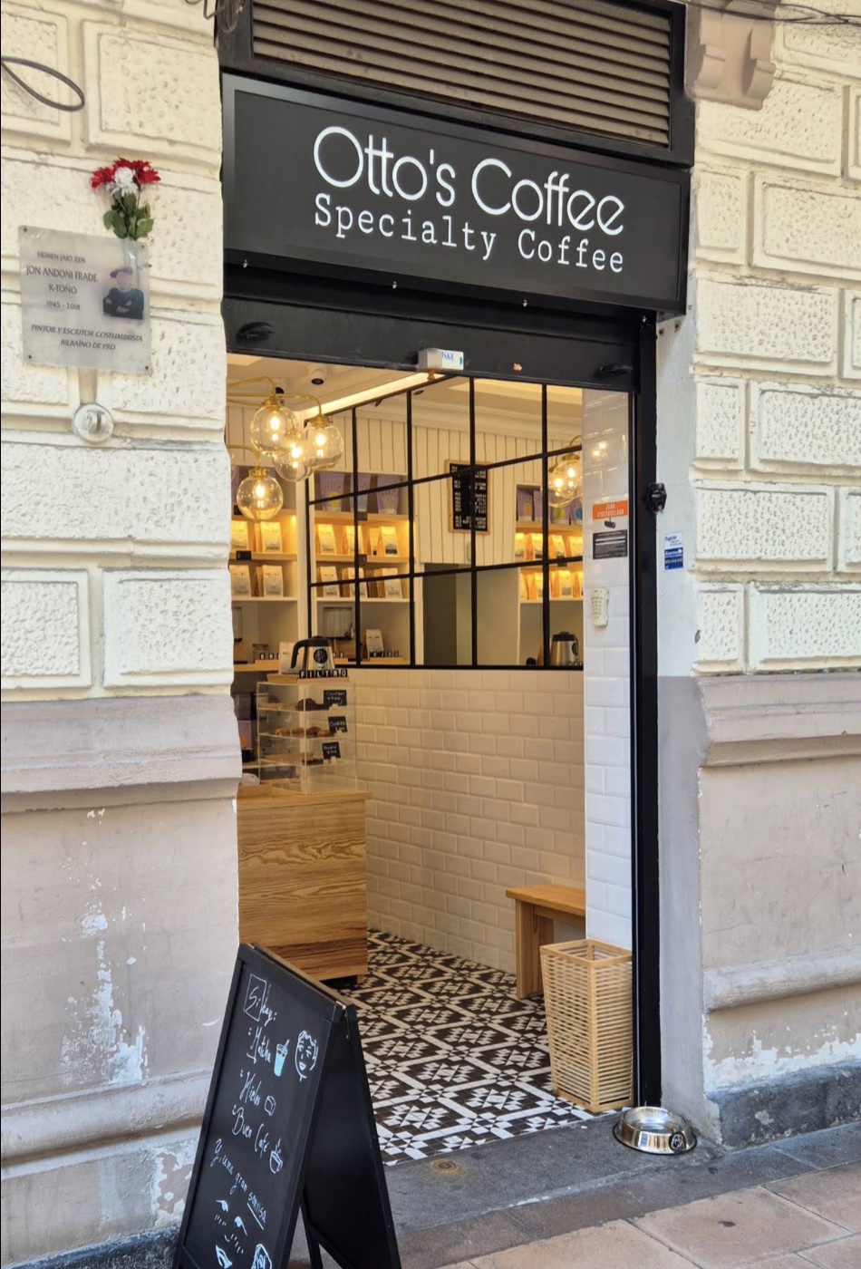La entrada de Otto's Coffee desde la acera, con la pizarra en la puerta y el cuenco de agua para perros